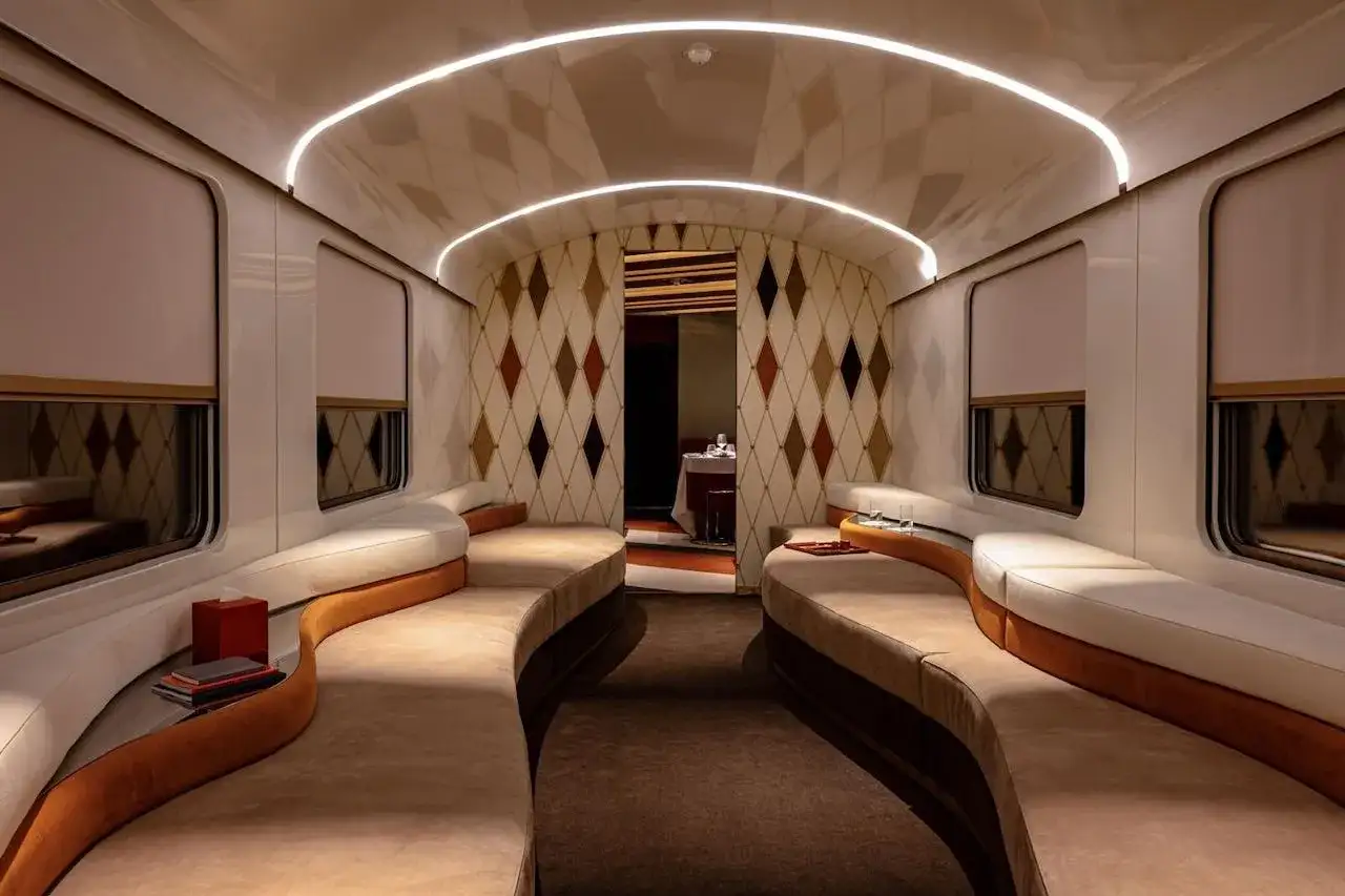 Luxuriöses Interieur eines Nachtzugs nach Italien mit geschwungenen Sofas, Rautenmuster-Tapete und indirekter Beleuchtung.