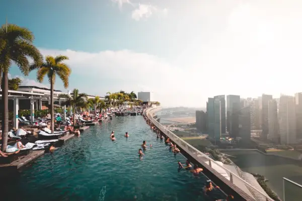 Menschen entspannen sich in einem Infinity-Pool mit Blick auf die Skyline von Singapur. Die **Singapur Regeln** für den Pool sind klar: Genießen!