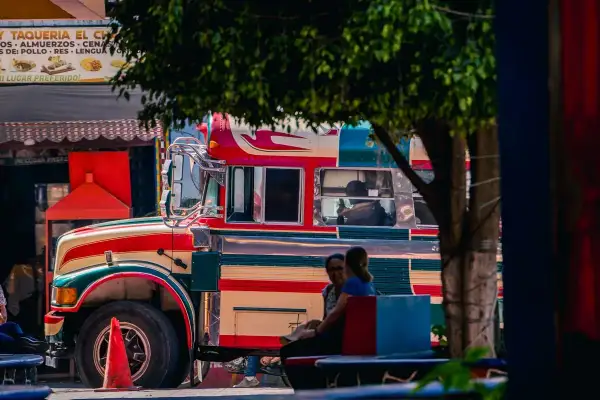 Bunter "chicken bus" in Guatemala, bereit für die nächste Fahrt. Menschen warten auf dem Bürgersteig.