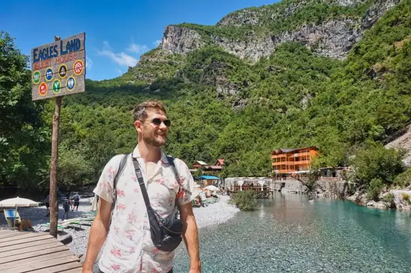 Ein Mann genießt die atemberaubende Landschaft Albaniens. Ein Schild weist auf "Eagles Land Guest House" hin, ein perfektes Ziel für Backpacking in Albanien.