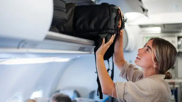 Junge Frau verstaut ihren großen Backpacking Rucksack im Gepäckfach eines Flugzeugs.