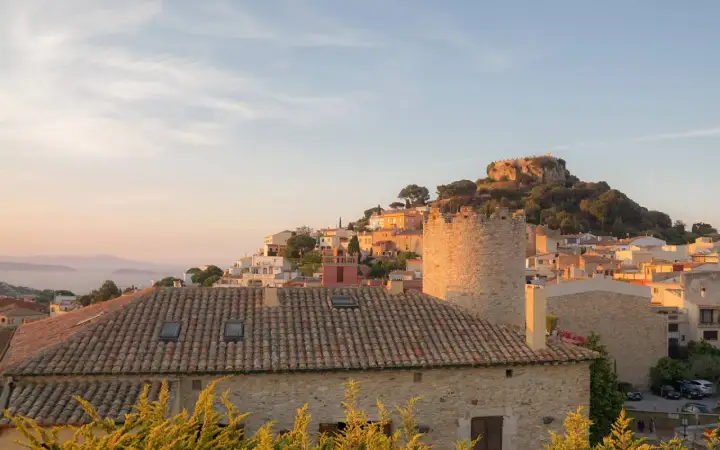 Sonnenuntergang über einem Dorf an der Girona Costa Brava. Ein alter Turm und ein Schloss auf einem Hügel über weiß getünchten Häusern.
